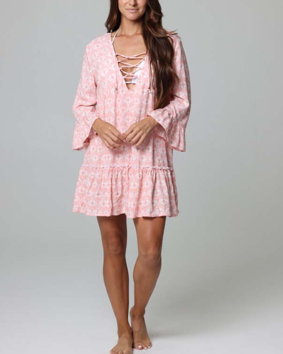 Model wearing a tiered cover up dress with a lace down detail in a pink and white print