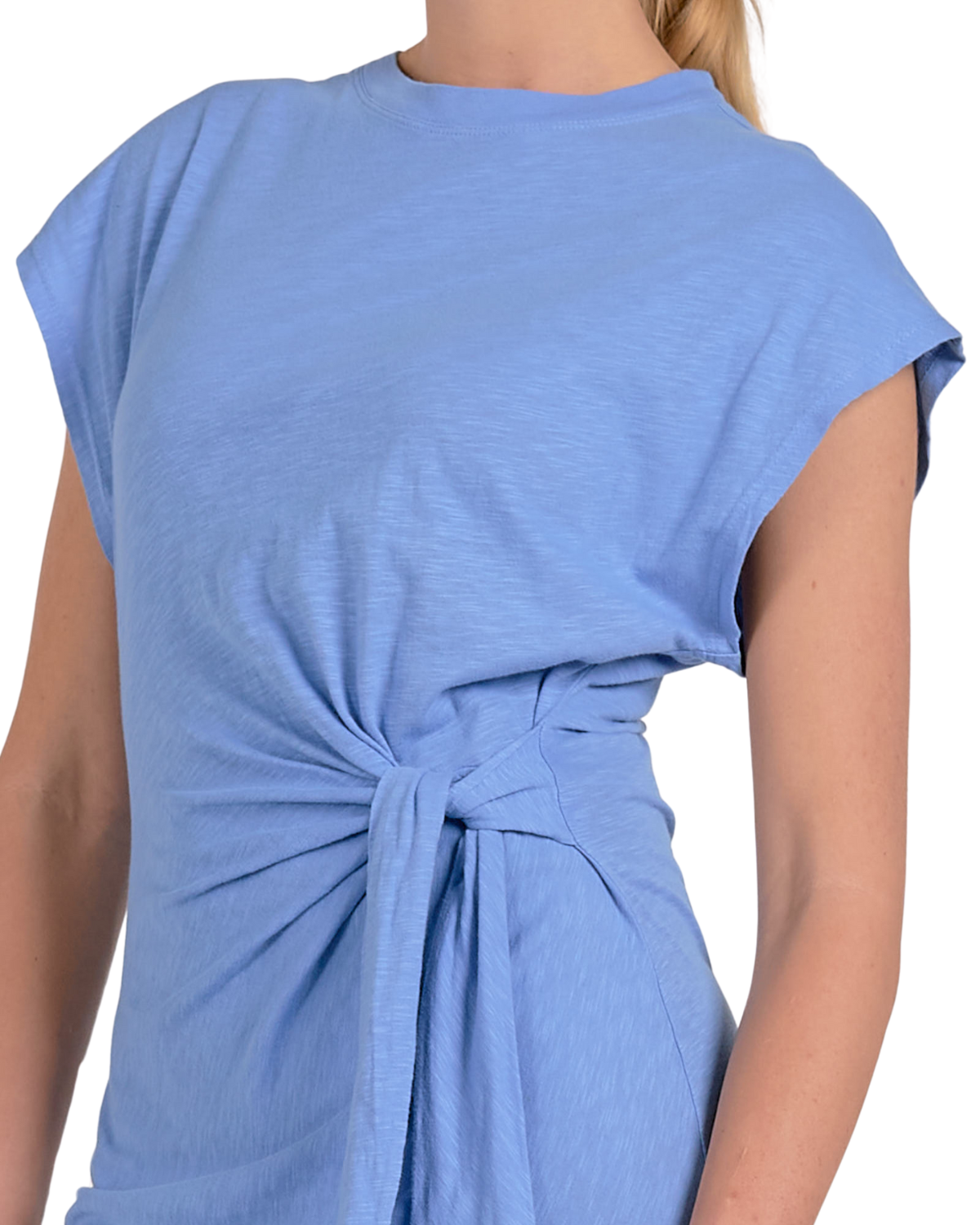 A woman wearing a light blue, short-sleeved midi dress made from a soft, jersey-like fabric. The dress features a crew neckline, a side tie detail at the waist creating a gathered effect, and a side slit for added movement. She completes the look with black buckle sandals and subtle stud earrings.