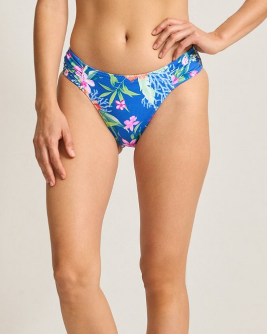 A reversible bikini bottom shown in two views. One side features a tropical floral print on a vibrant blue background, while the reverse side displays the same floral pattern on a bright yellow background. Both sides have a mid-rise fit with ruched detailing at the hips for a flattering silhouette. The design offers versatility and style in a sustainable swimwear option