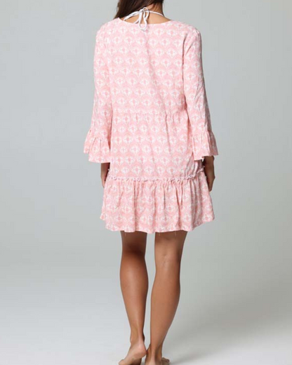 Model wearing a tiered cover up dress with a lace down detail in a pink and white print