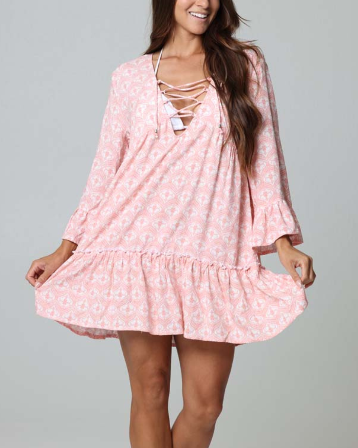 Model wearing a tiered cover up dress with a lace down detail in a pink and white print