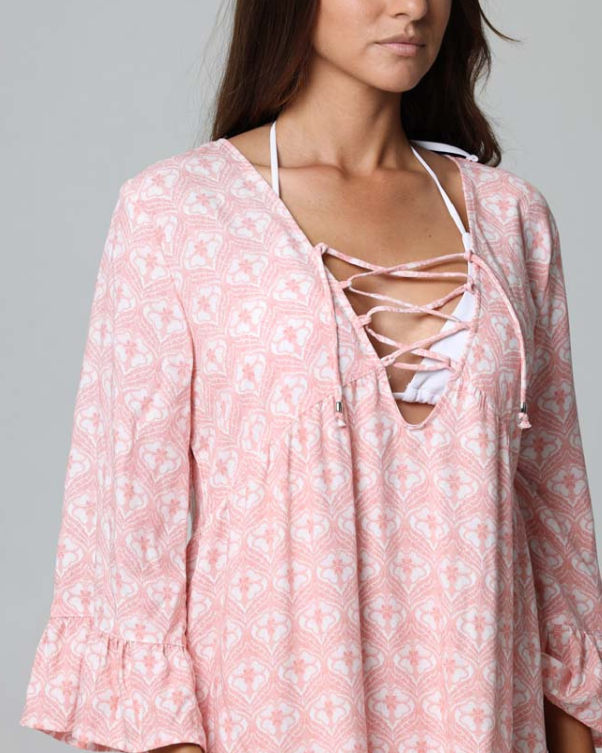 Model wearing a tiered cover up dress with a lace down detail in a pink and white print