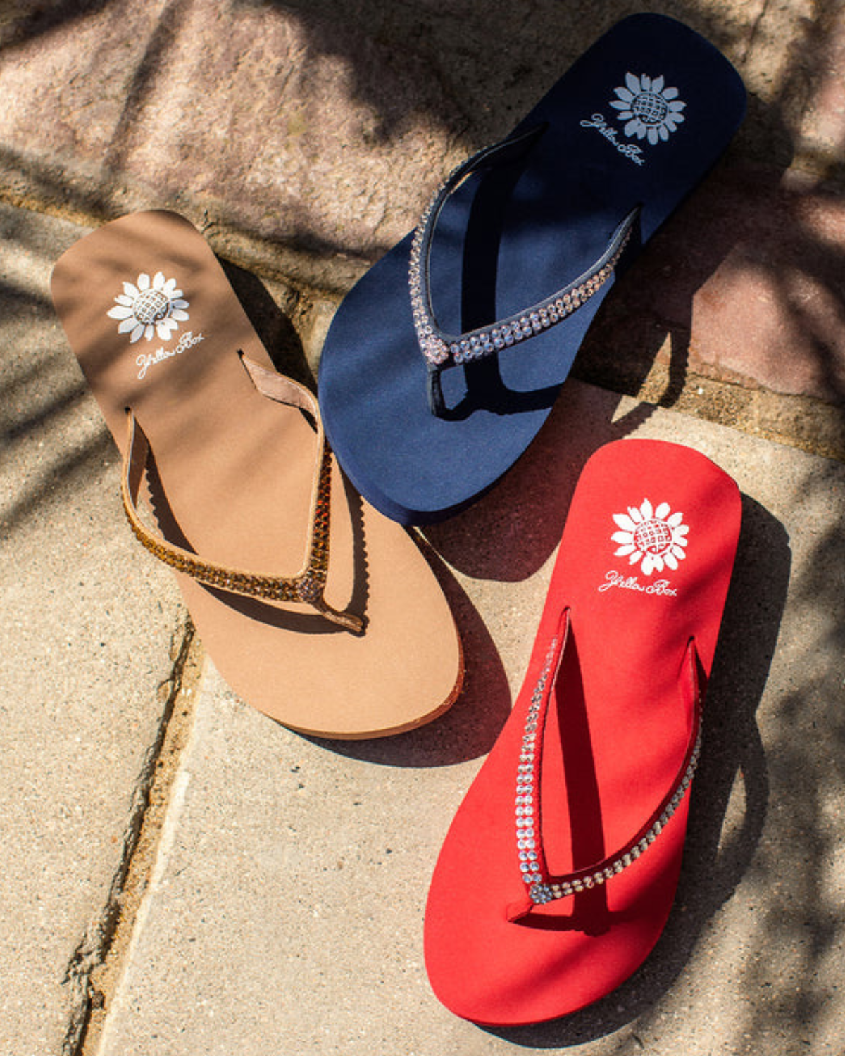 A group of women's multi colored wedge sandals with rhinestones on the strap. From left to right it shows taupe, navy, and red.
