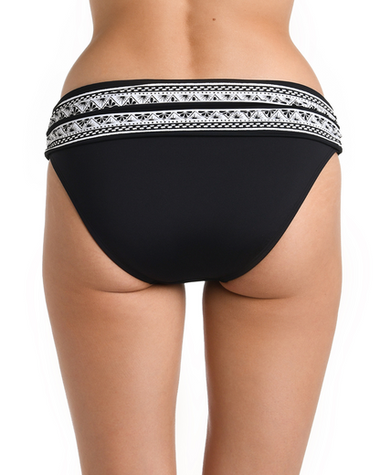 Model wearing a hipster banded bikini bottom in black with a white ornate print on the band