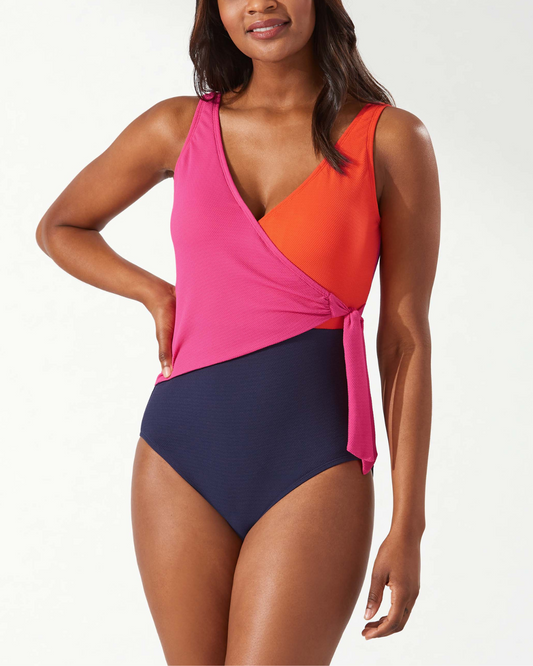 Model wearing a one piece wrap swimsuit in a colorblock print in navy, pink and red