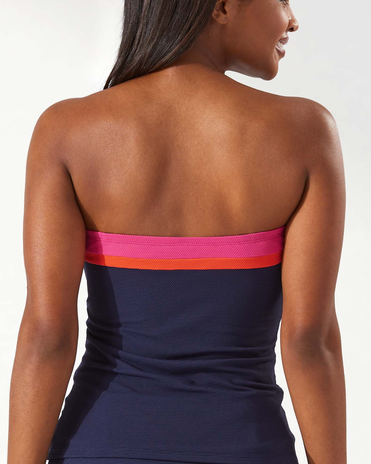 Model wearing a bandeau tankini top in navy with pink and orange stripes at the neckline