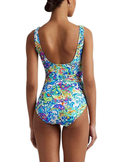 Model wearing a one piece swimsuit with a v-neck ruffle trim and shirred torso in a paisley blue, white, green and yellow multi colored print