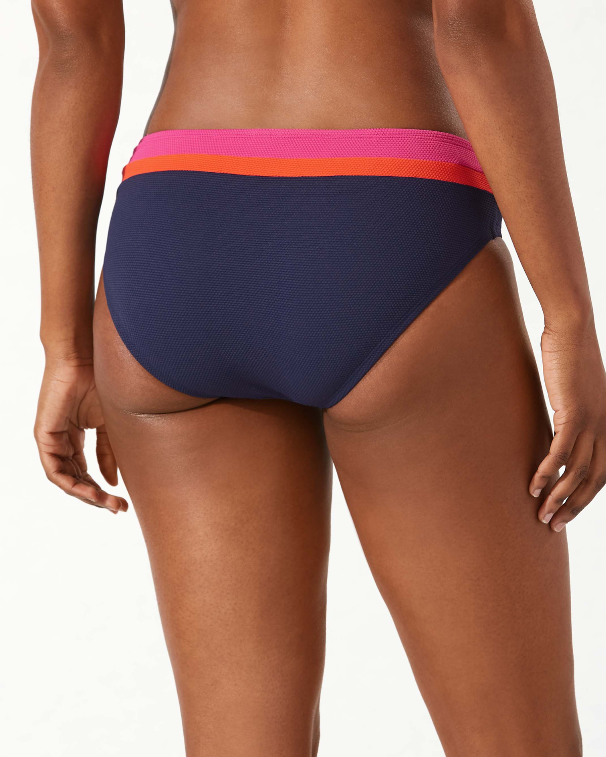 Model wearing a hipster bikini bottom in navy with a pink and orange stripe at the top