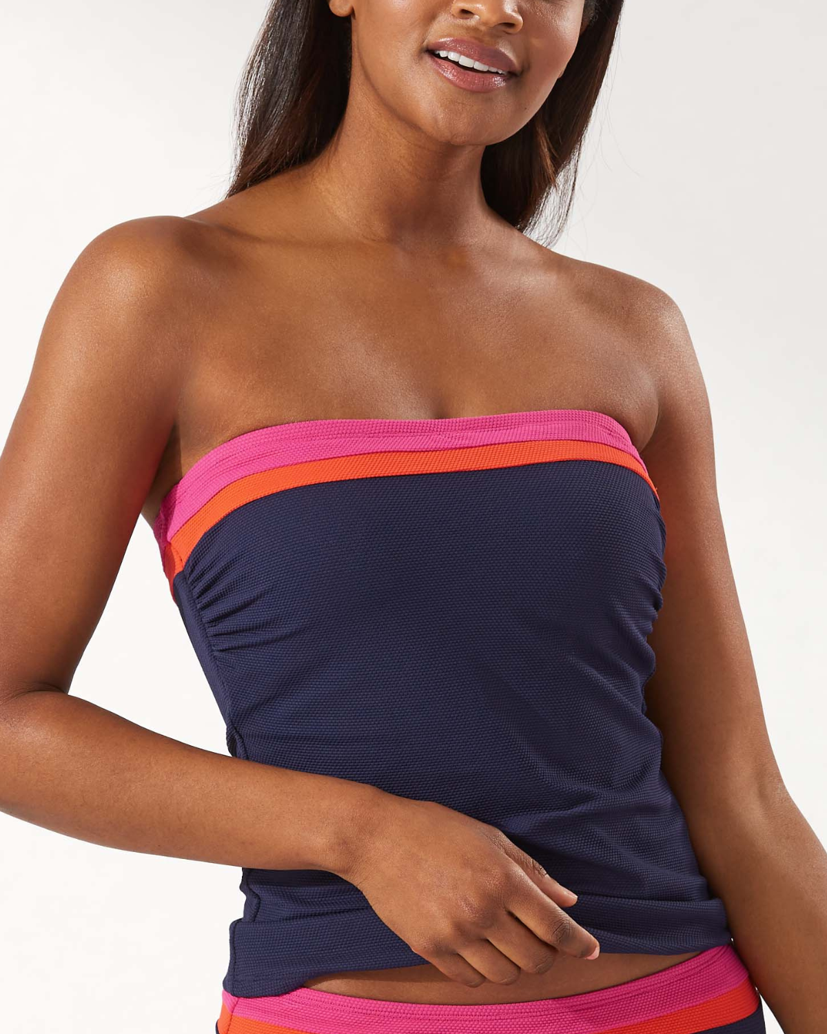 Model wearing a bandeau tankini top in navy with pink and orange stripes at the neckline