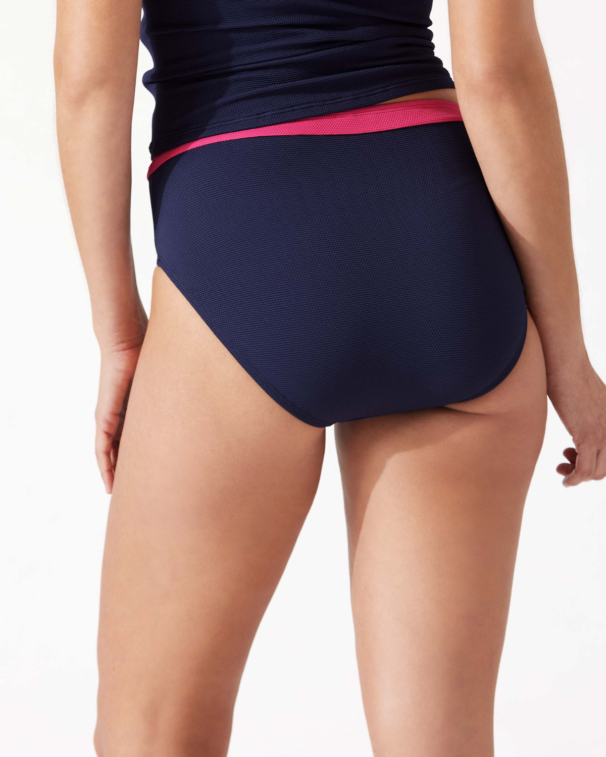 Model wearing a high waist bikini bottom in navy with a pink stripe at the top
