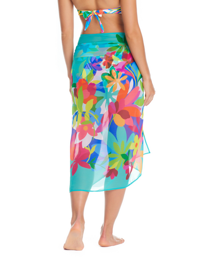 Model wearing a pareo cover up with a turquoise base and yellow, green, purple, blue, and white abstract floral details.