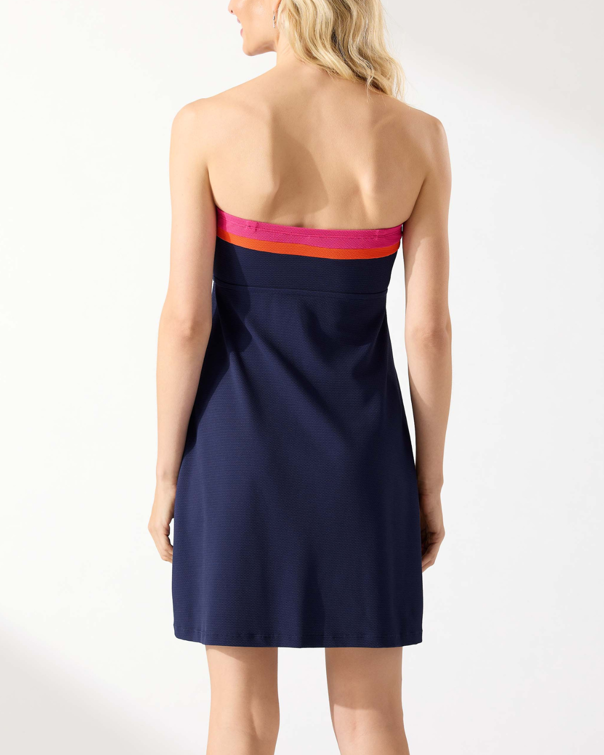 Model wearing a strapless bandeau spa dress with pockets in navy with a pink and orange stripe on the neckline
