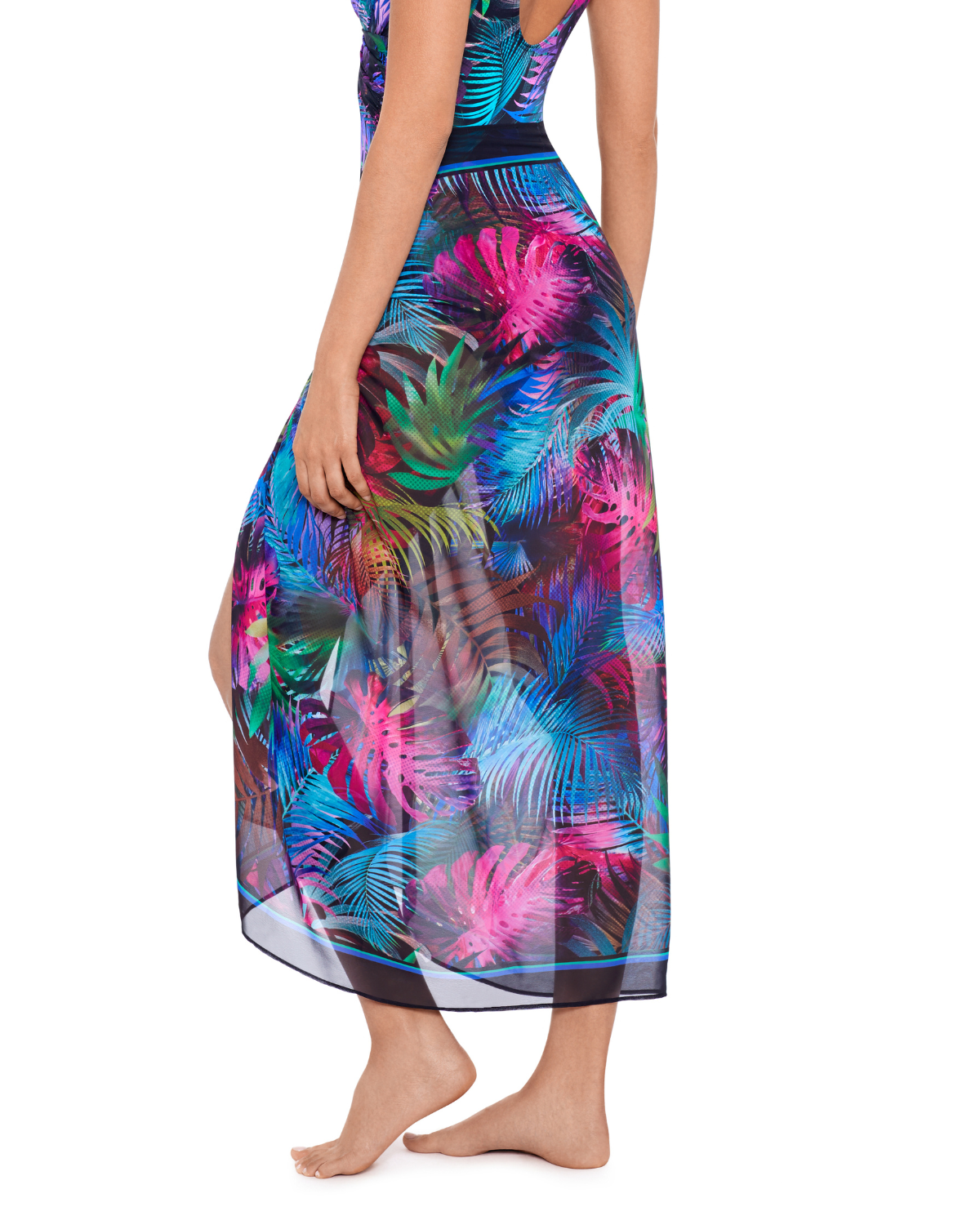 A model wearing a cover up pareo in a pink, green, blue, and black palm frond print