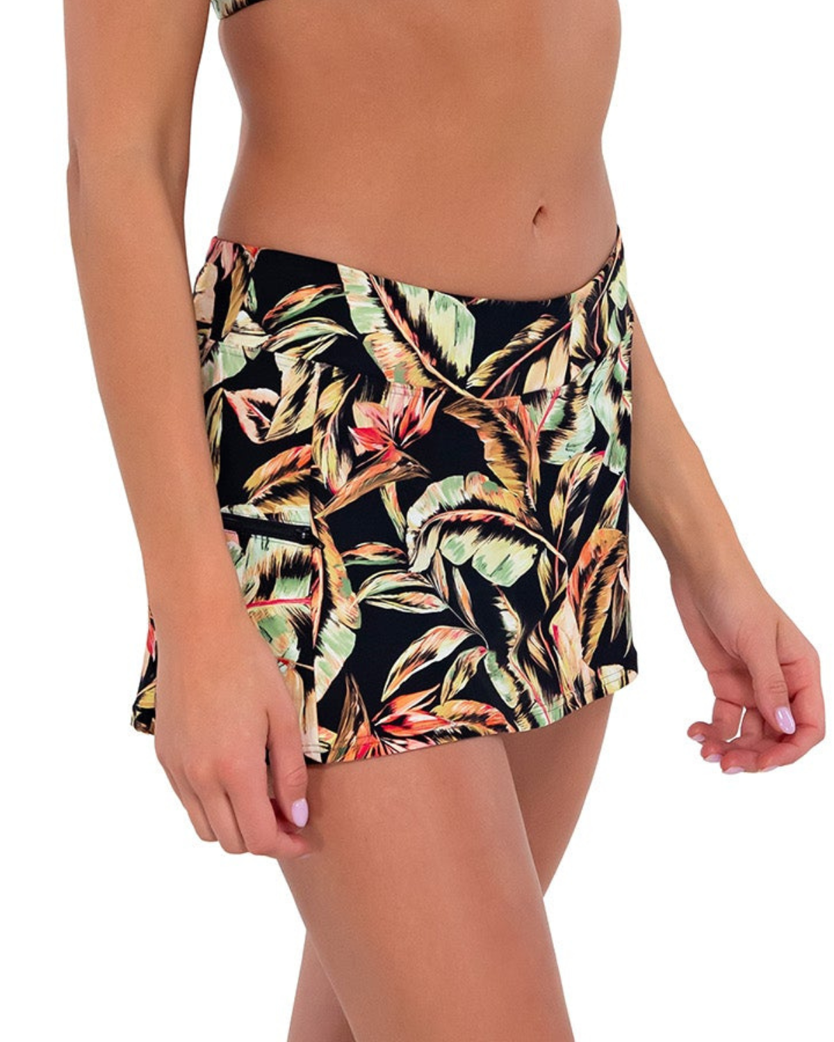 Model wearing a swim skirt with side pocket and hidden short in a black, green and red tropical print.