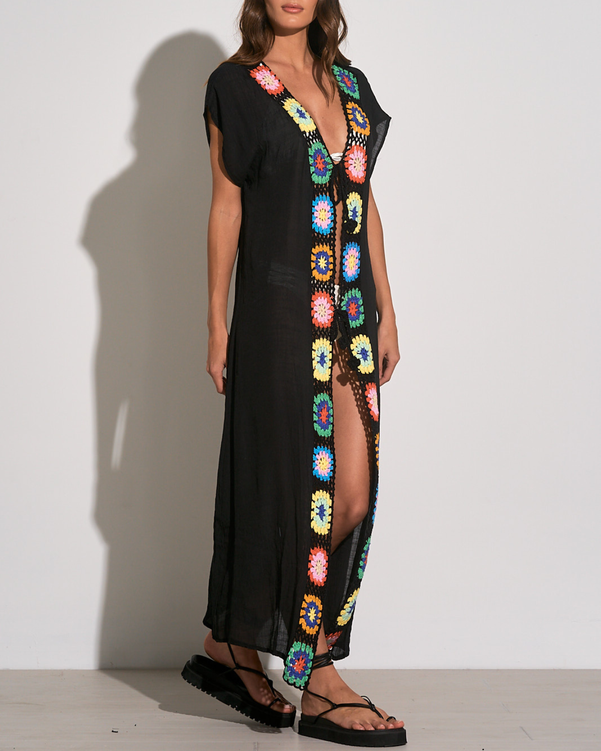 Model wearing a maxi length short sleeve kimono cover up with square crochet detail in black, green, yellow, blue, and orange