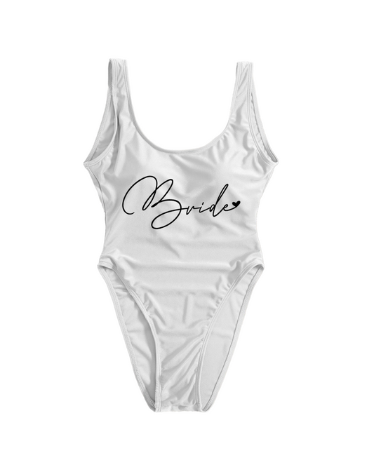Flat lay on a white backdrop of white one piece swimsuit with the word 'Bride' in a cursive black font 