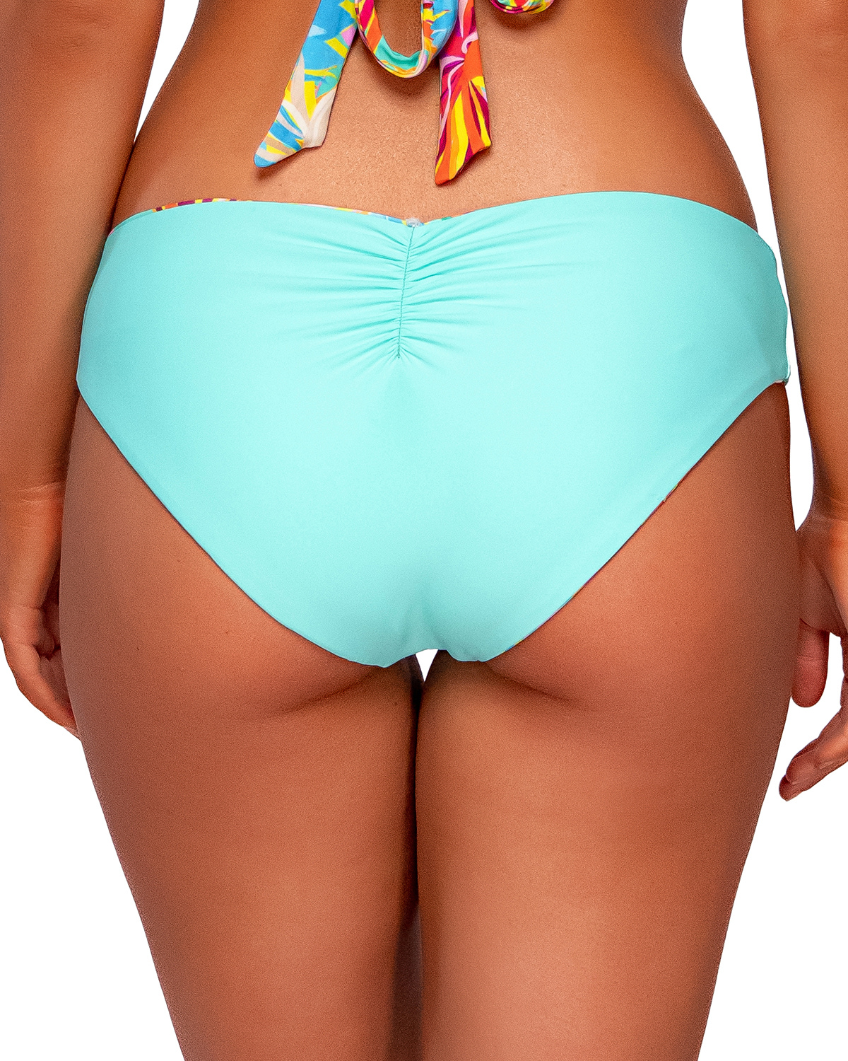 Model wearing a reversible hipster bikini bottom in a orange, yellow, turquoise and pink floral print. Bottom reverses to solid turquoise. 