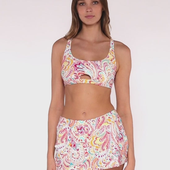 Model rotating 360 degrees wearing a swim skirt with side pocket and hidden short in a white, yellow, red, purple and turquoise paisley print with a matching bikini top.